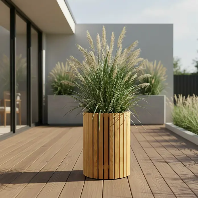 Andrewex Pflanzsäule rund Quadra - Außenmaß (Ø x H): 34 x 40 cm, Holz, Kiefer - Hölzerner Pflanzkübel mit Ziergras auf einer Terrasse. Der Kübel ist aus hellen Holzlatten gefertigt und steht auf einem Holzdeck.