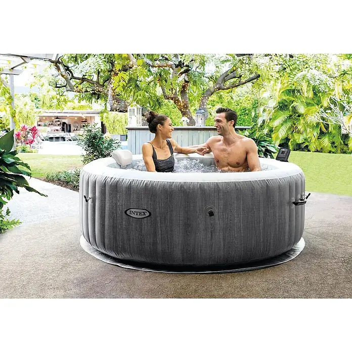 Intex Pure Spa Hidromasaje móvil Greenwood - Ø x Al: 196 x 71 cm, Gris/Blanco, 795 l - Bañera de hidromasaje inflable Intex en un jardín con una pareja relajándose y disfrutando de las burbujas.