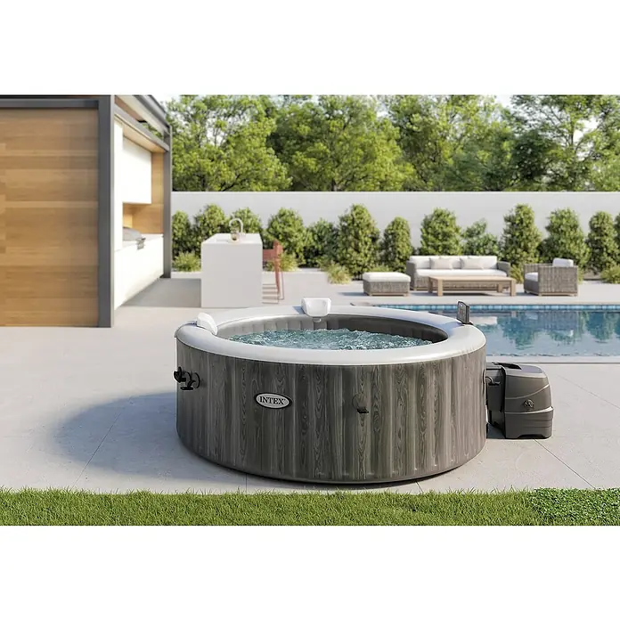 Intex Pure Spa Mobil-Whirlpool Greywood Deluxe Bubble - Ø x H: 196 x 71 cm, Grau, 795 l - Abbildung eines grauen Intex Whirlpools im Außenbereich mit Pool, Gartenmöbeln und Bäumen. Ideal für Entspannung im Garten!