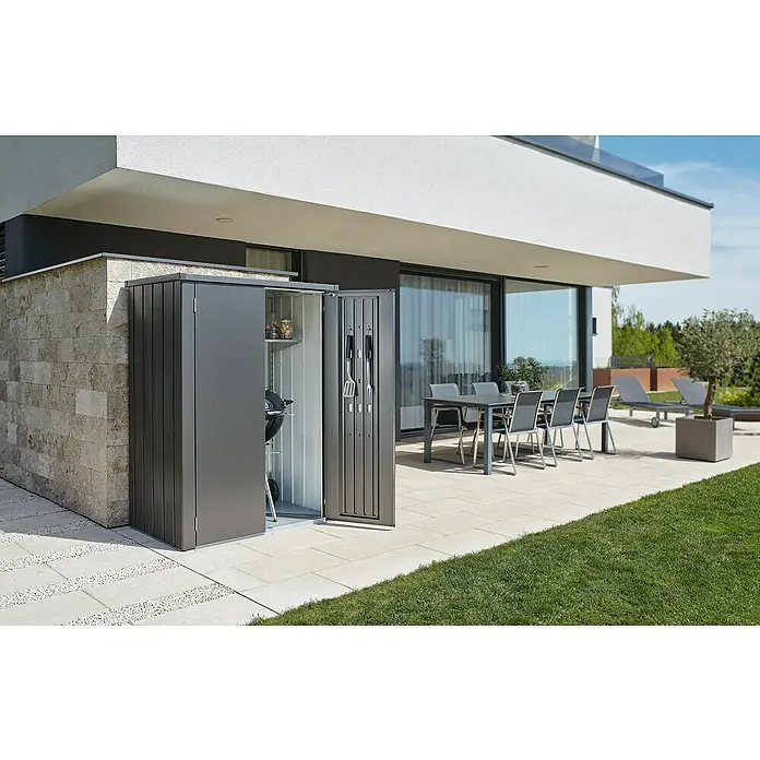 Biohort Romeo Gerätehaus - Außenmaß inkl. Dachüberstand (B x T): 132 x 87 cm, Stahl, Dunkelgrau-Metallic - Außenaufnahme eines Gerätehauses mit Grill und Zubehör neben einem modernen Haus mit Terrassenmöbeln.