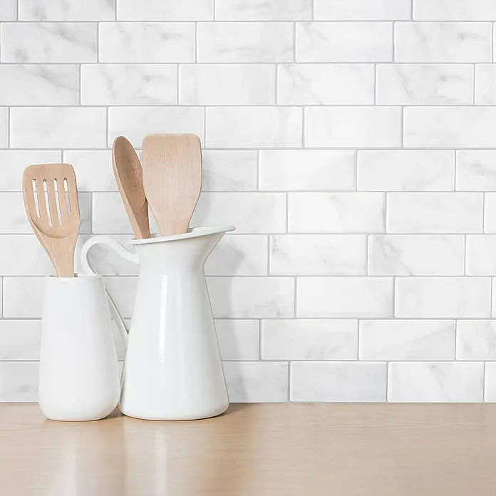 Smart Tiles Selbstklebemosaik Metro - 29,34 x 21,28 cm, Carrera, Glänzend - Nahaufnahme von zwei weißen Krügen mit Holzlöffeln vor einer weißen Marmorfliesenwand und einer Holzoberfläche.