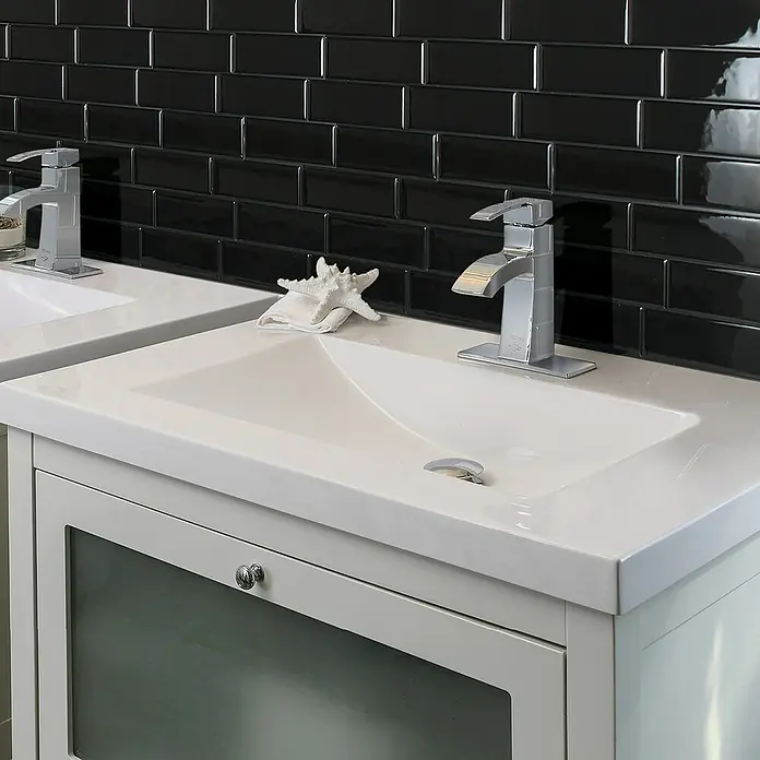 Smart Tiles Selbstklebemosaik Metro - 29,34 x 21,28 cm, Nero, Glänzend - Ein moderner Waschtisch mit zwei Becken und verchromten Armaturen vor einer schwarzen Metrofliesenwand.