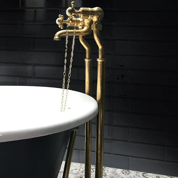 Smart Tiles Selbstklebemosaik Oslo - 57,31 x 27,62 cm, Nero, Glänzend - Nahaufnahme einer freistehenden Badewannenarmatur aus Messing mit einer dazugehörigen Zugkette vor einer dunklen, gefliesten Wand.