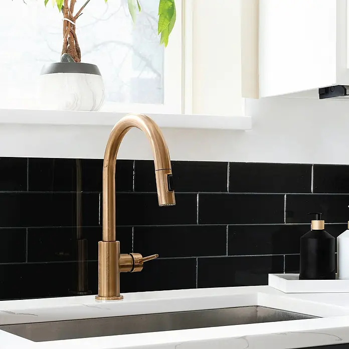 Smart Tiles Selbstklebemosaik Oslo - 57,31 x 27,62 cm, Nero, Glänzend - Nahaufnahme eines eleganten Küchenarmatur aus gebürstetem Gold, die einen Hauch von Luxus in die moderne Küchenspüle bringt.