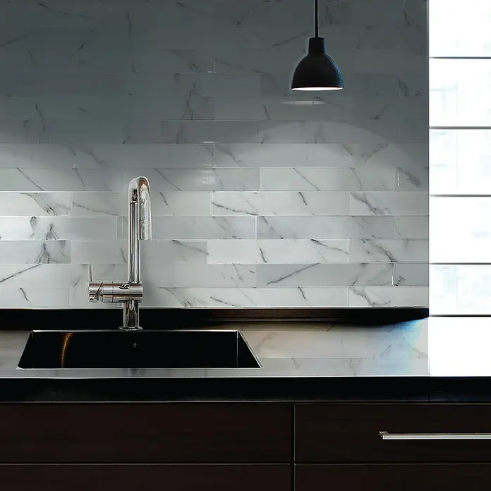 Smart Tiles Selbstklebemosaik Norway - 57,31 x 49,4 cm, Asti, Matt - Eine Nahaufnahme einer Küche mit glänzenden weißen Marmorfliesen an der Wand und einer stilvollen Armatur am Spülbecken.