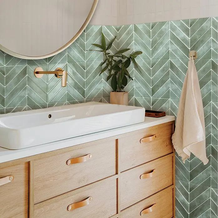 Smart Tiles Selbstklebemosaik Chevron - 29,02 x 22,86 cm, Solna, Glänzend - Ein stilvolles Badezimmer-Waschtisch mit hellen Holzschubladen, Ledergriffen und einem modernen, rechteckigen Waschbecken. Ein runder Spiegel ergänzt das Design.