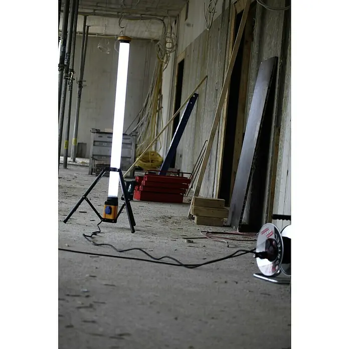 Profi Depot LED-Strahler L120 - 5.030 lm, 6.400 K, L x B x H: 74 x 85 x 158 cm, IP54 - Eine Arbeitsleuchte mit hellem LED-Licht steht auf einem Betonboden, umgeben von Baumaterialien.