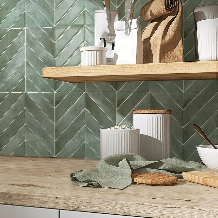 Smart Tiles Selbstklebemosaik Chevron - 29,02 x 22,86 cm, Solna, Glänzend - Nahaufnahme von grünen Ziegeln in Fischgrätmuster, die eine stilvolle Küchenrückwand bilden. Holzregal und Arbeitsfläche ergänzen das Design.