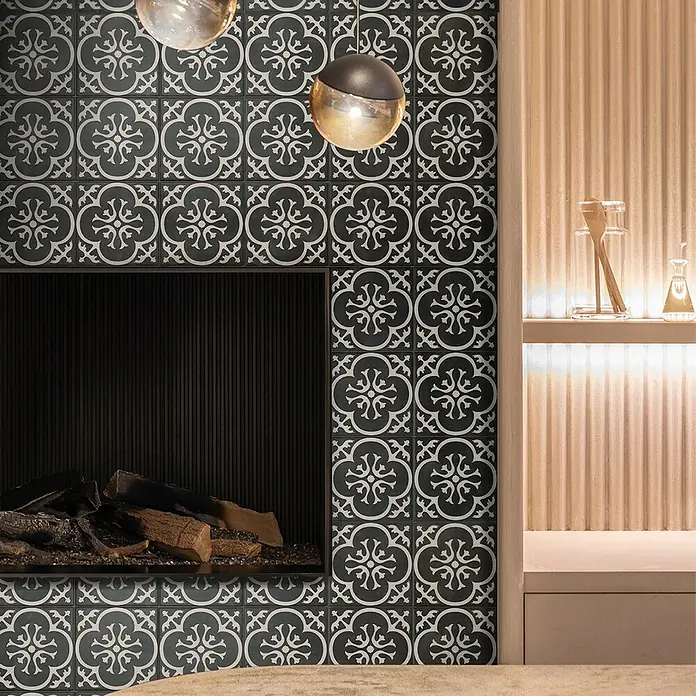 Smart Tiles Selbstklebemosaik Vintage - 19,69 x 19,69 cm, Girona Nera, Glänzend - Nahaufnahme eines Kamins mit dunkel gemusterten Fliesen und zwei hängenden Leuchten, die eine elegante und gemütliche Atmosphäre schaffen.