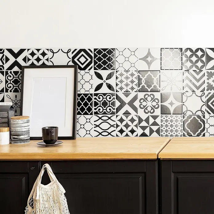 Smart Tiles Selbstklebemosaik Vintage - 22,86 x 22,86 cm, Bilbao, Glänzend - Nahaufnahme einer Küchenarbeitsplatte mit dekorativen Fliesen, einer Tasse und einem Bilderrahmen, die eine stilvolle und funktionale Küchengestaltung zeigen.