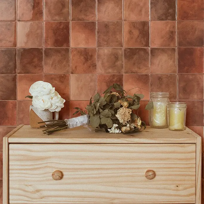 Smart Tiles Selbstklebemosaik Zellige - 22,86 x 22,86 cm, Safi, Glänzend - Dekorative Kommode aus hellem Holz mit Blumenstrauß und Kerzen, die eine warme und einladende Atmosphäre schafft.
