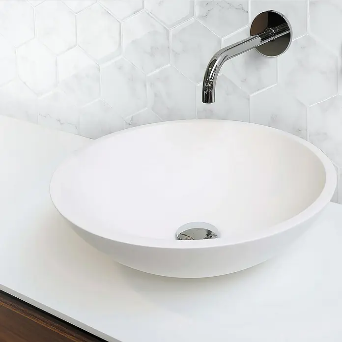 Smart Tiles Selbstklebemosaik Hexa - 24,78 x 23,75 cm, Yule, Glänzend - Elegantes Badezimmerwaschbecken mit einer glatten, runden Form und einem modernen, wandmontierten Wasserhahn. Die Marmorfliesen ergänzen das minimalistische Design.