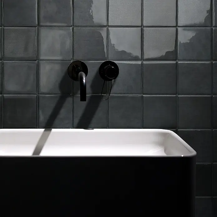 Smart Tiles Selbstklebemosaik Zellige - 22,86 x 22,86 cm, Taroudant, Glänzend - Moderne Badezimmerarmatur mit schwarzem Wasserhahn vor grauen Fliesen und einem eleganten Waschbecken.