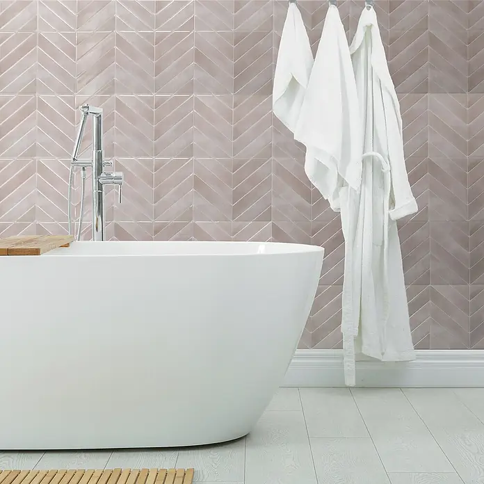 Smart Tiles Selbstklebemosaik Chevron - 29,02 x 22,86 cm, Viby, Glänzend - Elegantes Badezimmer mit freistehender Badewanne und stilvoller Wandfliese im Fischgrätmuster. Weiße Bademäntel hängen bereit.