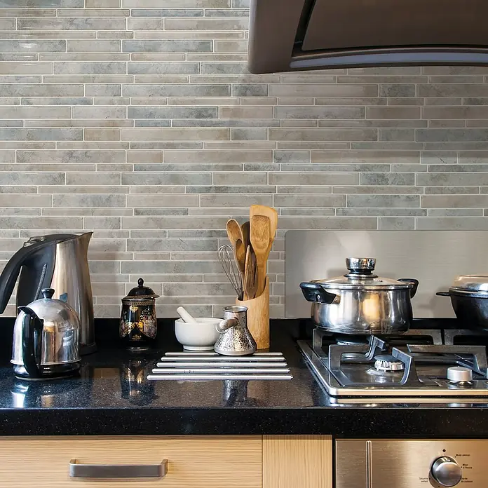 Smart Tiles Selbstklebemosaik Milano - 29,33 x 24,45 cm, Todi, Matt - Detailaufnahme einer Küche mit stilvoller grauer Backsteinmauer und diversen Küchenutensilien auf einer schwarzen Arbeitsplatte.