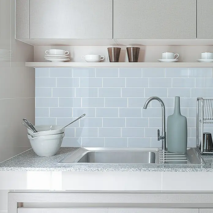 Smart Tiles Selbstklebemosaik Metro - 29,34 x 21,28 cm, Babe, Glänzend - Eine moderne Küche mit einem Edelstahlspülbecken unter einem hellblauen Fliesenspiegel, umgeben von Geschirr und einer eleganten Vase.