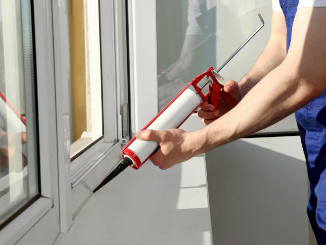 Mann silikoniert zwischen Fenster und Fensterbank