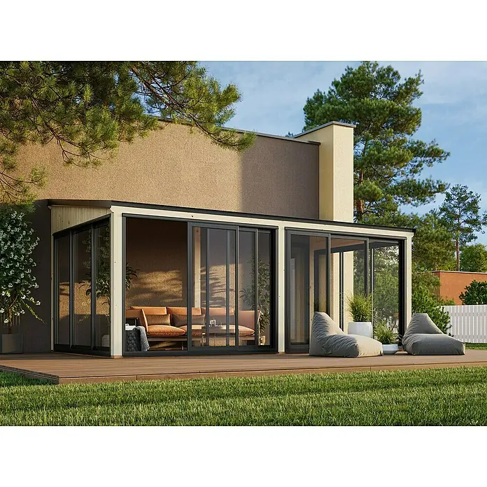 Palmako Pérgola adosada Lumi Slide Plus - L x An: 297 x 582 cm, Natural, Doble acristalamiento de 24 mm, Puerta corredera - Un elegante jardín de invierno con puertas correderas y modernos asientos en una terraza de madera, rodeado de exuberante vegetación.