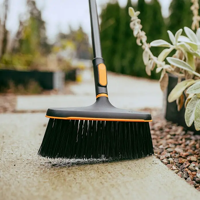 Fiskars OneClick Gartenbesen - Passend für: Fiskars OneClick-Stiel - Nahaufnahme eines schwarzen Fiskars Kehrbesens mit orangefarbenen Akzenten, der auf einer Betonoberfläche steht.