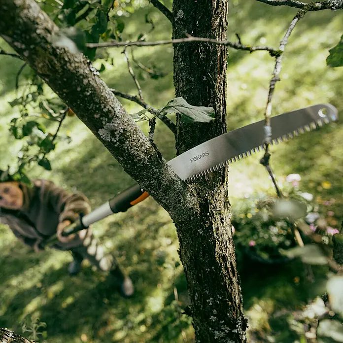 Fiskars OneClick Baumsäge - Passend für: Fiskars OneClick Stiel, Länge: 60,3 cm - Nahaufnahme einer Fiskars Astsäge beim Beschneiden eines Baumes im Garten, fokussiert auf die Säge und den Schnitt.