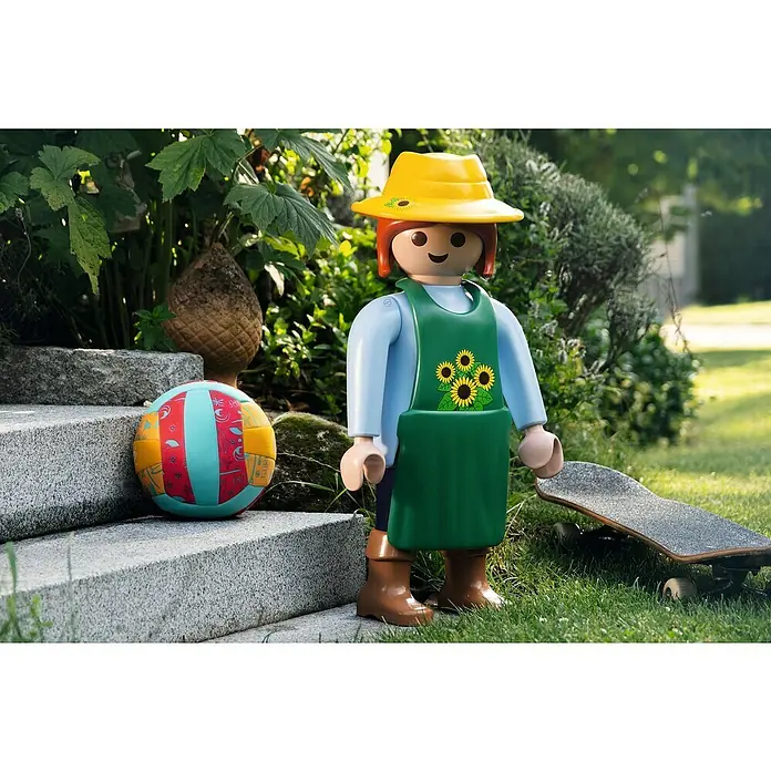 Lechuza Dekofigur Playmobil - Gärtnerin/Sonnenblume, L x B x H: 24 x 31 x 68 cm, Kunststoff - Detailaufnahme einer Playmobil-Gärtnerin mit gelbem Hut, grünem Overall und braunen Stiefeln neben einem bunten Ball und einem Skateboard.