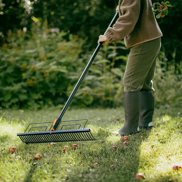 Fiskars OneClick Rasenrechen - L x B x H: 12,5 x 57 x 12,6 cm - Eine Person, die mit einem Laubbesen Fallobst vom Rasen aufliest, um den Garten aufzuräumen.