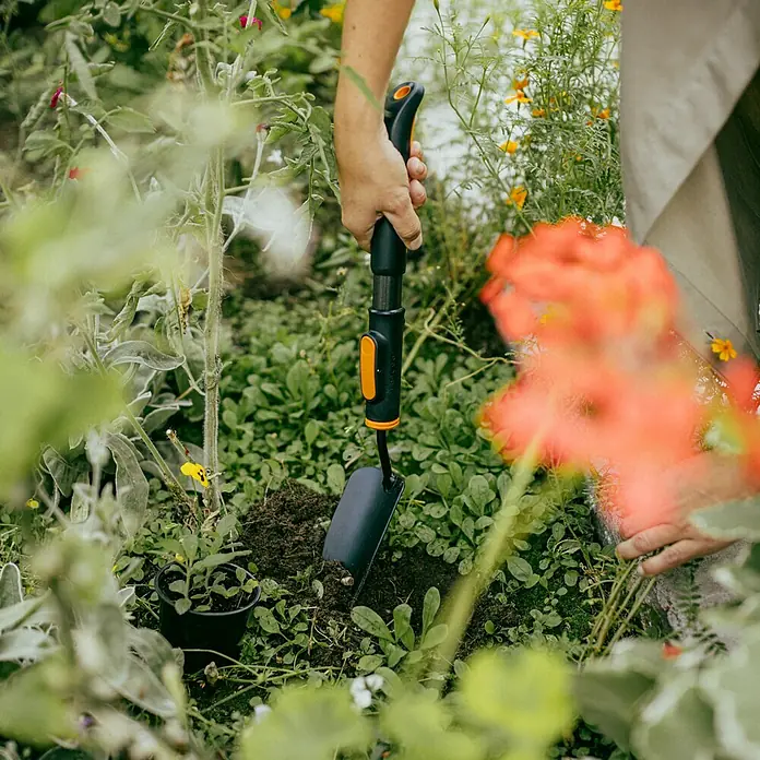 Fiskars OneClick Blumenkelle - 28,8 cm - Nahaufnahme einer Person, die mit einer Handschaufel im Garten arbeitet, um ein Loch für eine neue Pflanze zu graben.