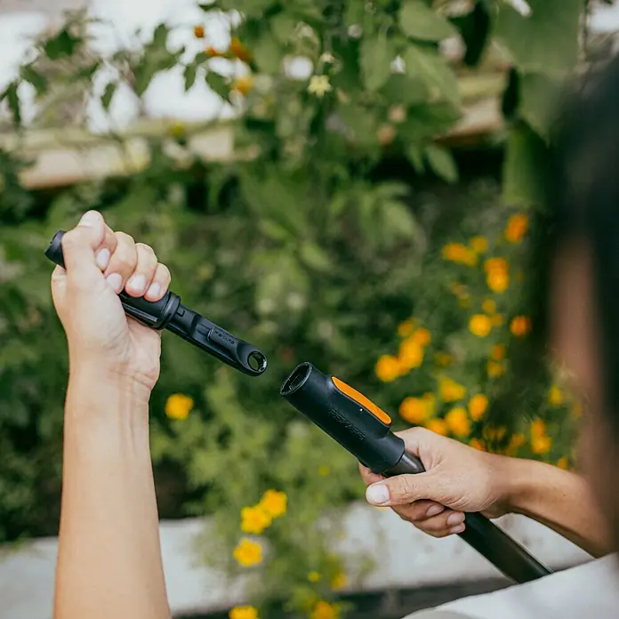 Fiskars OneClick Stiel - Passend für: Handgeräte der QuikFit™-Produktreihe - Nahaufnahme einer Person, die zwei Teile eines schwarzen Fiskars-Gartengeräts vor dem Zusammenfügen hält.