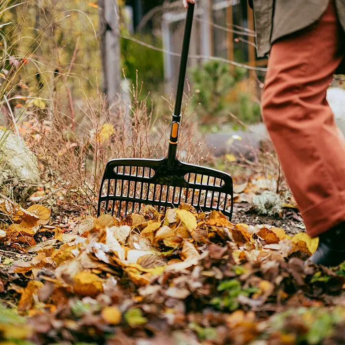 Fiskars OneClick Gartenrechen - Arbeitsbreite: 48,2 cm - Gartenarbeit mit einem Laubrechen, der auf einem Haufen bunter Herbstblätter liegt.