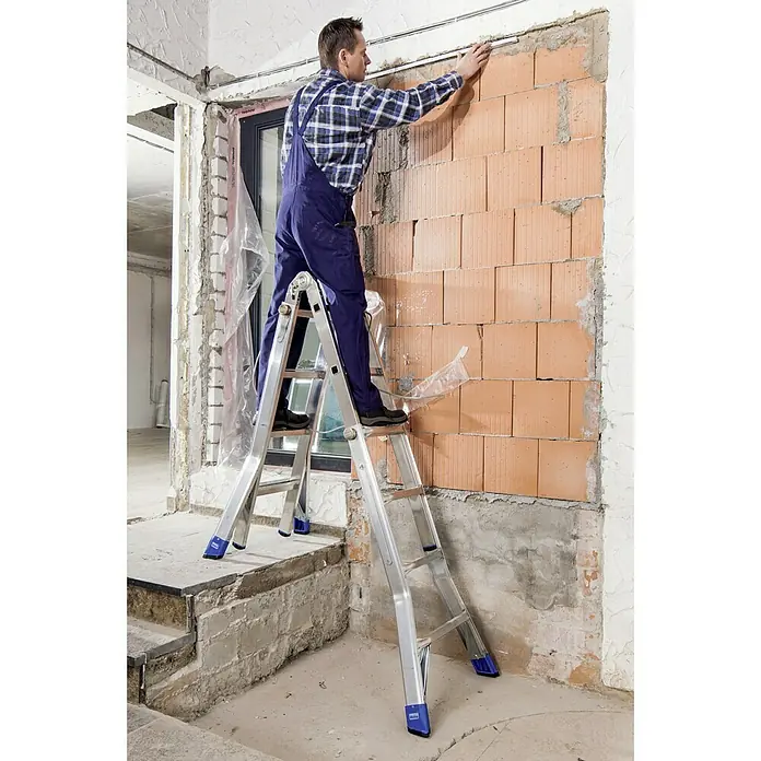 Krause Stabilo Teleskopleiter - Anzahl Tritte: 16 Stk., Arbeitshöhe: 5 m, Aluminium - Ein Handwerker benutzt eine Klappleiter von Krause, um an einer Ziegelwand zu arbeiten. Die Leiter steht stabil auf unterschiedlichen Ebenen.