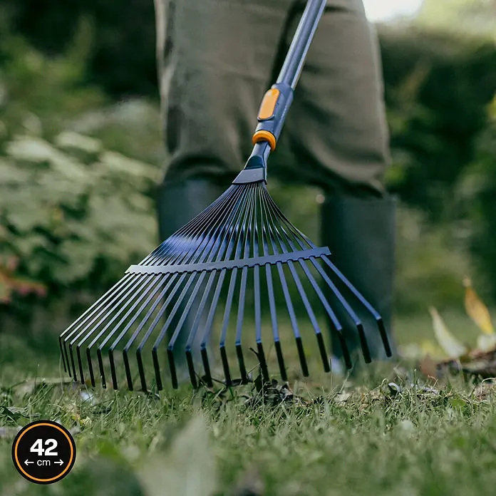 Fiskars OneClick Rasenrechen - L x B x H: 47,5 x 40 x 10,4 cm - Nahaufnahme eines Fiskars-Laubrechens mit verstellbarer Breite auf einer grünen Rasenfläche mit Laub.