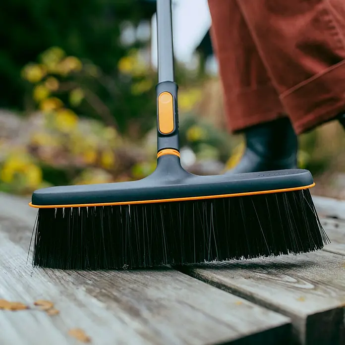 Fiskars OneClick Besen - Passend für: Fiskars OneClick-Stiel - Der Fiskars Kehrbesen mit orangenen Akzenten wird auf einem Holzsteg verwendet. Ideal für die Reinigung von Außenbereichen.