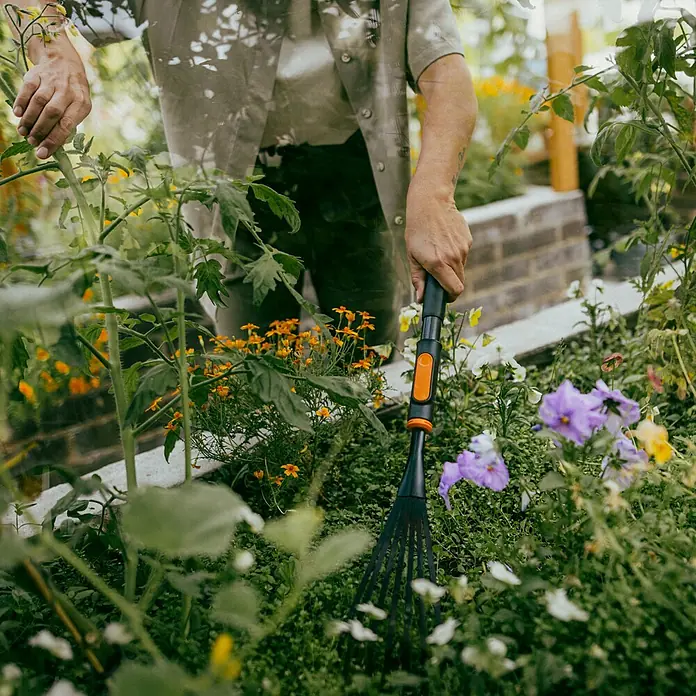 Fiskars OneClick Gartenrechen - Arbeitsbreite: 12,4 cm, Anzahl Zinken: 7 Stk. - Eine Person, die mit einem Gardena Fächerbesen im Garten arbeitet, um Laub und Pflanzenreste zu entfernen.