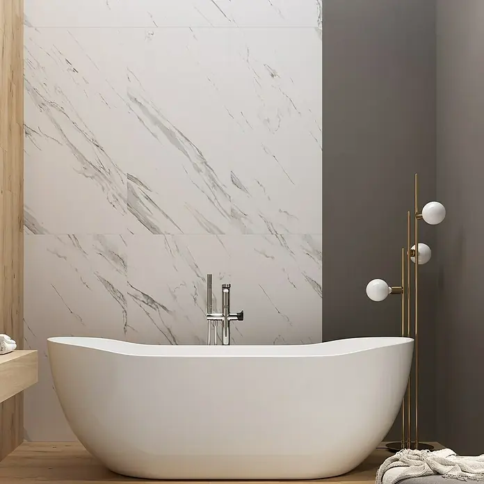 Feinsteinzeugfliese Calaccata Mistari - 59,8 x 119,8 cm, Weiß, Seidenmatt - Elegantes Badezimmer mit freistehender Badewanne, Marmorfliesen und goldener Stehlampe. Die Badewanne ist das zentrale Element des Bildes.