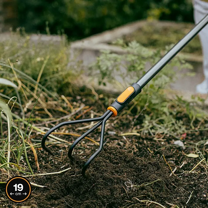 Fiskars OneClick Grubber - Arbeitsbreite: 13,2 cm, Anzahl Zinken: 3 Stk. - Nahaufnahme einer dreizinkigen Gartenhacke, die in dunkler Erde steckt, mit der Angabe ihrer Breite von 19 cm.