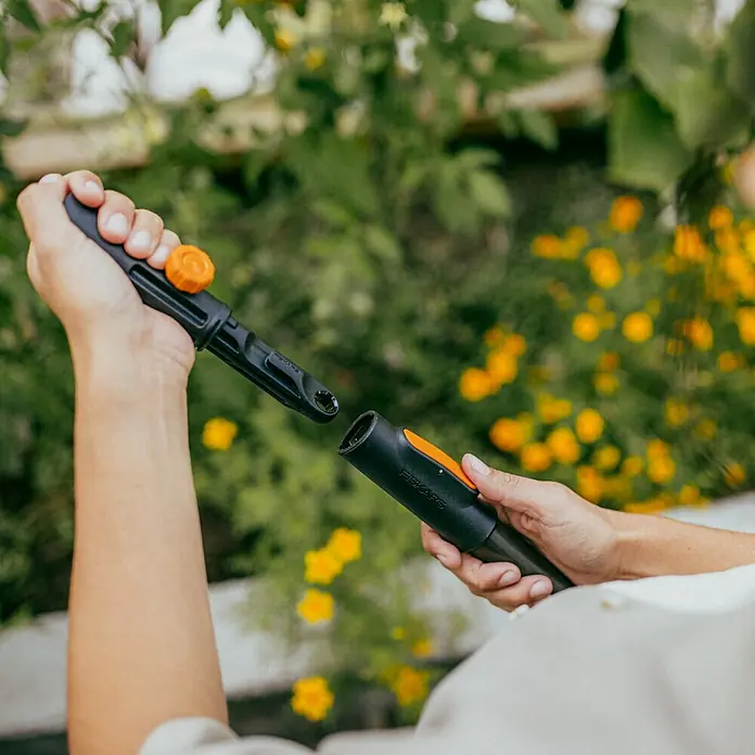 Fiskars OneClick Stiel Universal - Passend für: Handgeräte der QuikFit™-Produktreihe - Nahaufnahme einer Person, die eine schwarze Fiskars-Gartengeräteverlängerung mit orangefarbenen Akzenten zusammenbaut.