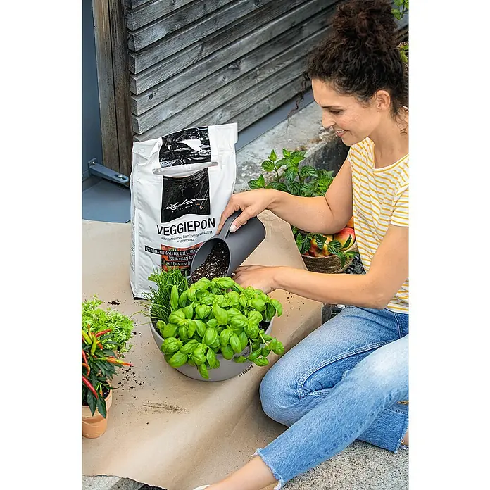 Lechuza Pflanzgranulat Veggiepon - 6 l - Eine Frau befüllt einen Topf mit Veggiepon-Gemüseerde, um Kräuter und Gemüse anzupflanzen. Ideal für den eigenen Garten.