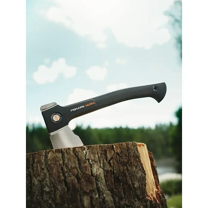 Fiskars Spaltaxt - Länge: 35,5 cm, 0,529 kg - Eine Fiskars Ultra Axt steckt in einem Baumstumpf, vor einem verschwommenen Hintergrund aus Grün und blauem Himmel.