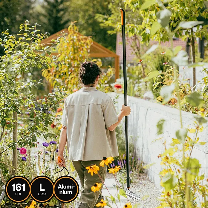 Fiskars OneClick Aluminiumstiel - Aluminium, 161,3 cm - Eine Frau hält einen schwarzen Aluminium-Unkrautstecher in einem üppigen Garten, umgeben von Blumen und Grün.