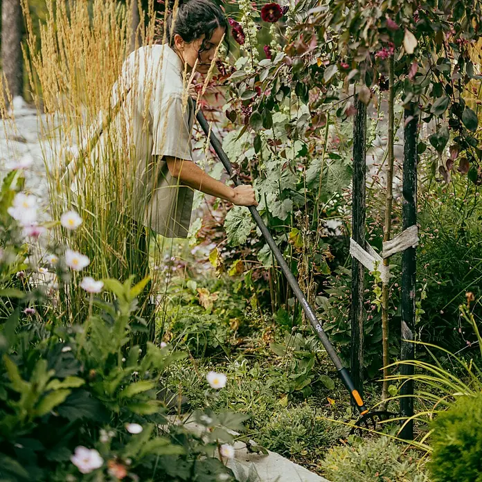 Fiskars OneClick Holzstiel - Passend für: Fiskars Quikfit Stecksystem, 140 cm - Frau benutzt einen Fiskars Kultivator im Garten, um Blumen und Pflanzen zu pflegen.
