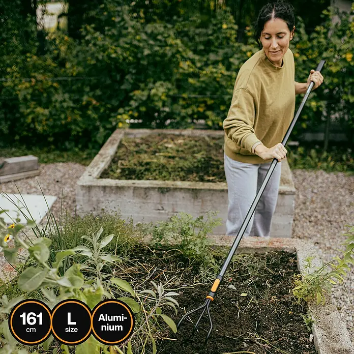 Fiskars OneClick Aluminiumstiel - Aluminium, 161,3 cm - Eine Frau benutzt einen langen Unkrautstecher von Fiskars in einem Gartenbeet. Der Stecher hat einen Aluminiumschaft und eine Länge von 161 cm.