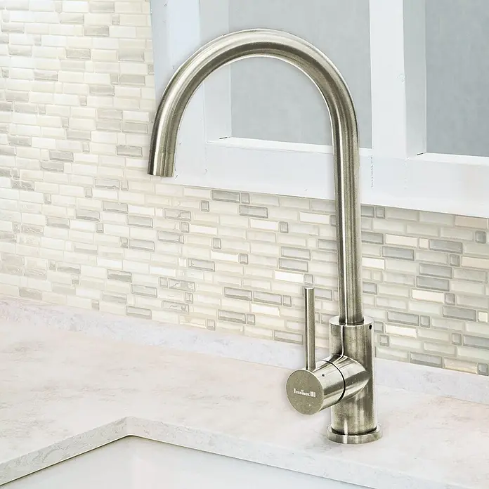 Smart Tiles Selbstklebemosaik Crescendo - 24,69 x 23,77 cm, Ciotta, Glänzend - Nahaufnahme einer eleganten Edelstahl Küchenarmatur vor einer stilvollen Fliesenwand und einem weißen Fenster.