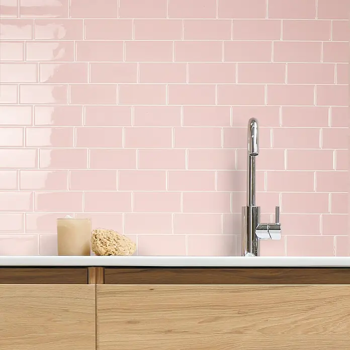 Smart Tiles Selbstklebemosaik Metro - 29,34 x 21,28 cm, Ava, Glänzend - Nahaufnahme von glänzenden, rosafarbenen Metrofliesen an einer Küchenwand, kombiniert mit einer stilvollen Armatur und einer hellen Arbeitsplatte.