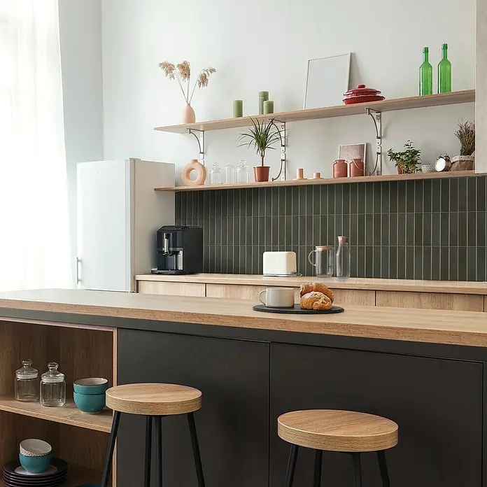 Smart Tiles Selbstklebemosaik Morocco - 29,02 x 22,86 cm, Toulal, Matt - Küchenaufnahme mit einer Arbeitsplatte aus Holz, darunter schwarze Schränke und zwei Barhocker. Regale mit Deko und Geräten vervollständigen das Bild.