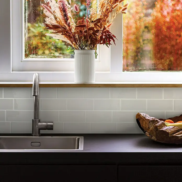 Smart Tiles Selbstklebemosaik Metro - 29,34 x 21,28 cm, Cassandra, Glänzend - Nahaufnahme einer modernen Küche mit Spüle, Armatur und einer weißen Vase mit Blumen vor einem Fenster.