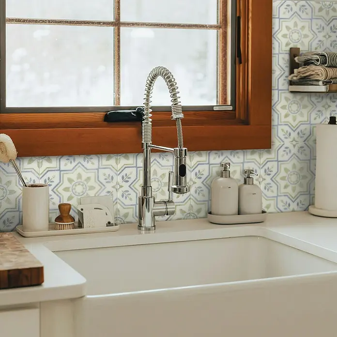 Smart Tiles Selbstklebemosaik Vintage - 22,86 x 22,86 cm, Augusta, Glänzend - Nahaufnahme einer Spüle mit Armatur, Seifenspendern und gemusterten Fliesen im Hintergrund, die eine einladende Küchenatmosphäre schaffen.