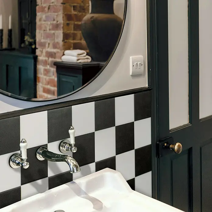 Smart Tiles Selbstklebemosaik Betera - 19,69 x 19,69 cm, Paris, Matt - Nahaufnahme eines Badezimmers mit einem Waschbecken mit Wasserhahn, schwarz-weiß karierten Fliesen und einem Spiegel.