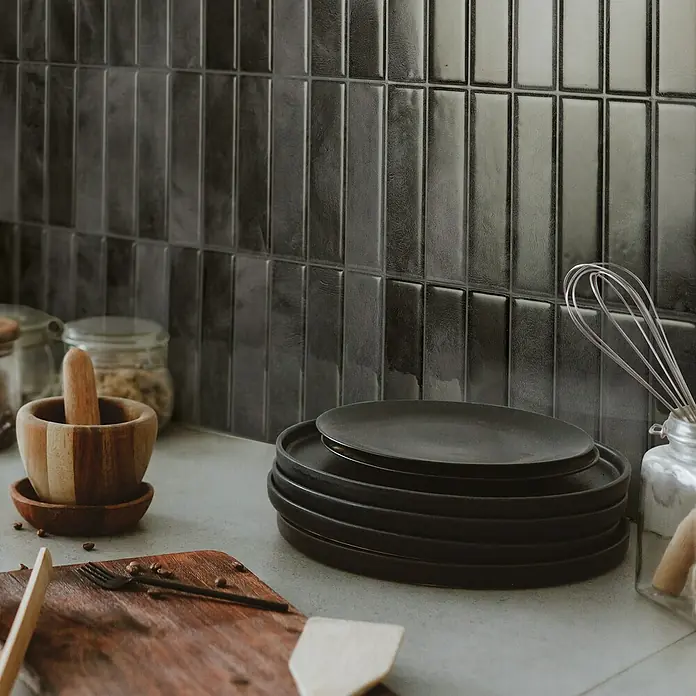 Smart Tiles Selbstklebemosaik Morocco - 29,02 x 22,86 cm, Zaida, Glänzend - Nahaufnahme von schwarzen Tellern, einer Holzschale mit Stößel und Küchenutensilien vor einem Hintergrund mit dunklen, rechteckigen Fliesen.