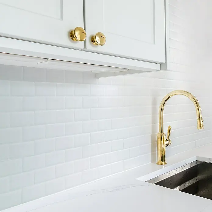 Smart Tiles Selbstklebemosaik Subway - 27,81 x 24,64 cm, White, Glänzend - Küchenarmatur aus Gold mit passenden Knöpfen an weißen Schränken, die ein elegantes und stilvolles Design zeigen.