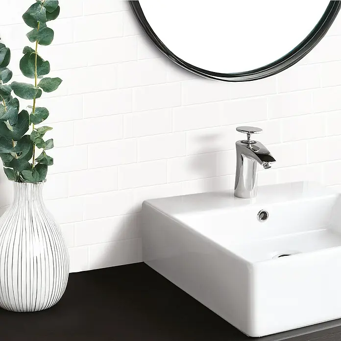 Smart Tiles Selbstklebemosaik Metro - 29,34 x 21,28 cm, Blanco, Glänzend - Ein modernes Badezimmerwaschbecken mit stilvollem Wasserhahn, ergänzt durch eine elegante Vase und einem Spiegel. Helle und saubere Ästhetik.